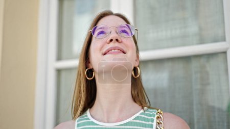 Foto de Joven mujer rubia sonriendo confiada mirando al cielo en la calle - Imagen libre de derechos