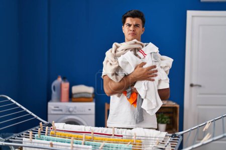 Foto de Hombre hispano colgando ropa en tendedero escéptico y nervioso, frunciendo el ceño molesto debido a un problema. persona negativa. - Imagen libre de derechos