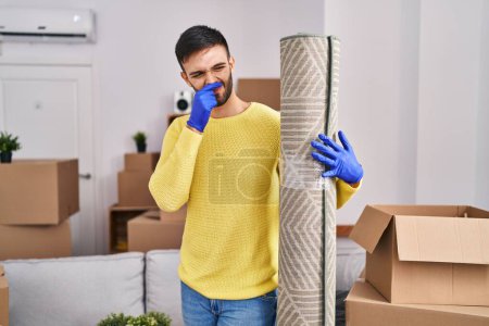 Photo for Young hispanic man smelling dirty carpet at new home - Royalty Free Image