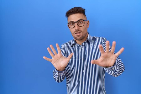 Téléchargez les photos : Homme hispanique avec barbe portant des lunettes peur et terrifié par l'expression de la peur arrêter geste avec les mains, criant en état de choc. concept de panique. - en image libre de droit