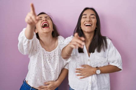 Foto de Madre e hija hispanas juntas riéndose de ti, señalando con el dedo a la cámara con la mano sobre el cuerpo, expresión de vergüenza - Imagen libre de derechos