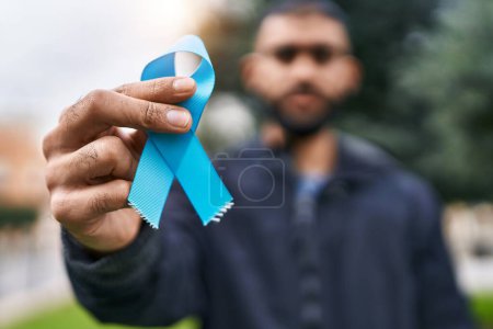 Foto de Young hispanic man holding light blue ribbon at park - Imagen libre de derechos