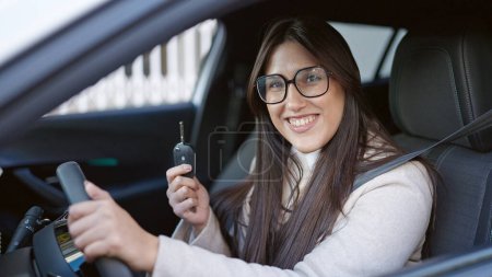 Téléchargez les photos : Jeune belle femme hispanique souriant confiance tenant la clé de la nouvelle voiture à la rue - en image libre de droit