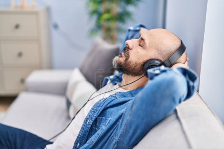 Téléchargez les photos : Jeune chauve écoutant de la musique détendue sur le canapé à la maison - en image libre de droit