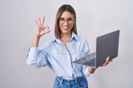 Foto de Mujer joven que trabaja con computadora portátil sonriendo positiva haciendo signo de ok con la mano y los dedos. expresión exitosa. - Imagen libre de derechos