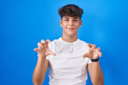 Photo for Hispanic teenager standing over blue background smiling funny doing claw gesture as cat, aggressive and sexy expression - Royalty Free Image