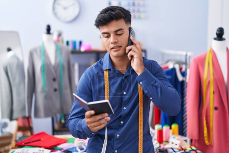Téléchargez les photos : Jeune homme hispanique tailleur parler sur le portable de lecture smartphone à l'usine de vêtements - en image libre de droit