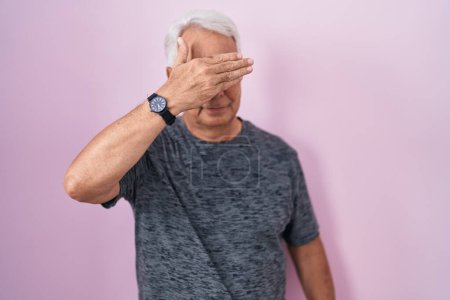 Photo for Middle age man with grey hair standing over pink background covering eyes with hand, looking serious and sad. sightless, hiding and rejection concept - Royalty Free Image