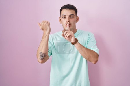 Photo for Handsome hispanic man standing over pink background asking to be quiet with finger on lips pointing with hand to the side. silence and secret concept. - Royalty Free Image
