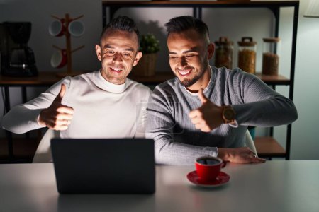 Téléchargez les photos : Couple homosexuel utilisant ordinateur portable approuvant faire geste positif avec la main, pouces levés souriant et heureux pour le succès. geste gagnant. - en image libre de droit