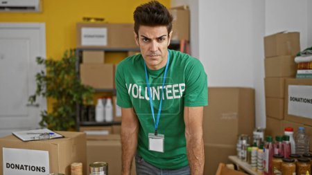 Photo for Young hispanic man volunteer standing with serious face at charity center - Royalty Free Image