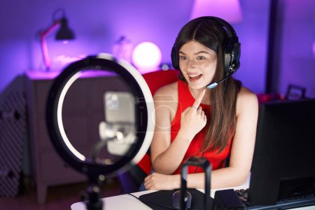 Téléchargez les photos : Jeune femme caucasienne jouant à des jeux vidéo enregistrement avec smartphone souriant heureux pointant avec la main et le doigt - en image libre de droit