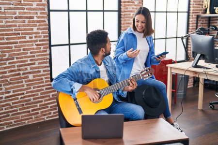Photo for Man and woman musicians playing classical guitar using smartphone at music studio - Royalty Free Image