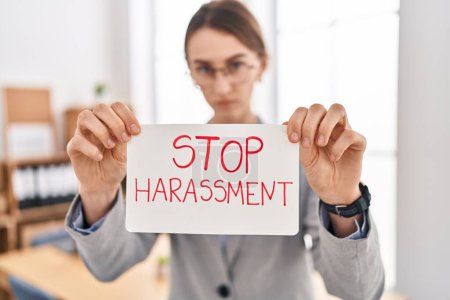 Téléchargez les photos : Jeune femme caucasienne travailleur d'affaires tenant arrêter la bannière de message de harcèlement au bureau - en image libre de droit
