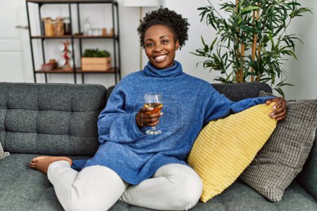 Photo for African american woman drinking glass of wine sitting on table at home - Royalty Free Image