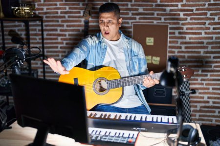 Photo for Hispanic young man playing classic guitar at music studio doing stop gesture with hands palms, angry and frustration expression - Royalty Free Image