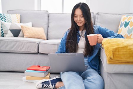 Téléchargez les photos : Jeune femme chinoise utilisant un ordinateur portable boire du café à la maison - en image libre de droit