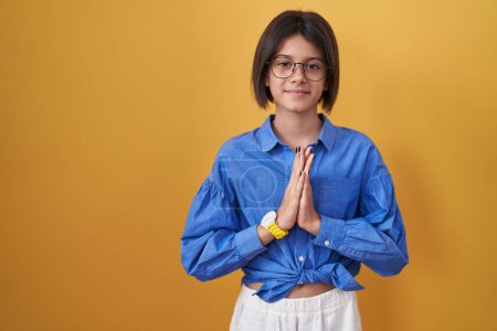 Photo for Young girl standing over yellow background praying with hands together asking for forgiveness smiling confident. - Royalty Free Image