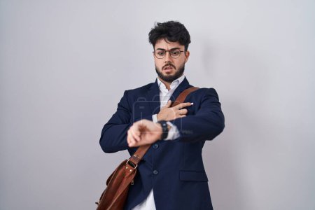 Téléchargez les photos : Homme hispanique avec barbe portant des vêtements de travail en regardant l'heure de la montre inquiet, peur de se faire tard - en image libre de droit