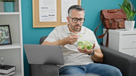 Foto de Hombre de pelo gris trabajador de negocios comiendo ensalada en la oficina - Imagen libre de derechos
