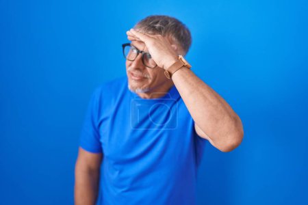 Photo for Hispanic man with grey hair standing over blue background very happy and smiling looking far away with hand over head. searching concept. - Royalty Free Image