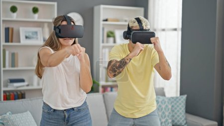 Téléchargez les photos : Beau couple jouant au jeu vidéo de boxe en utilisant des lunettes de réalité virtuelle à la maison - en image libre de droit