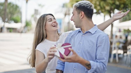 Téléchargez les photos : Belle surprise de couple avec boîte cadeau coeur souriant à la rue - en image libre de droit