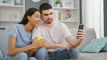 Téléchargez les photos : Beau couple amoureux, souriant en toute confiance, textos sur smartphone autour d'un café sur canapé salon à la maison - en image libre de droit