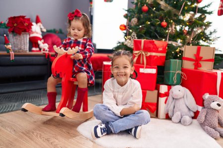 Foto de Hermano y hermana jugando con renos meciéndose en el árbol de Navidad en casa - Imagen libre de derechos