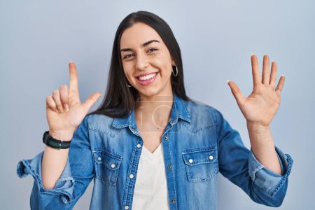 Téléchargez les photos : Femme hispanique debout sur fond bleu montrant et pointant vers le haut avec les doigts numéro sept tout en souriant confiant et heureux. - en image libre de droit