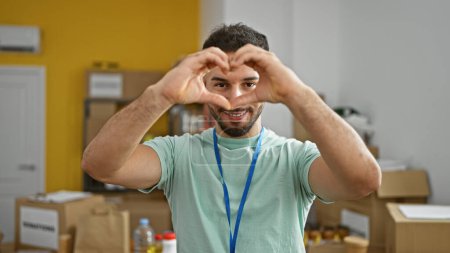 Téléchargez les photos : Jeune homme arabe bénévole faisant geste de coeur souriant au centre de charité - en image libre de droit
