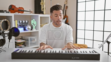 Photo for Handsome young hispanic man, a musical artist, passionately playing acoustic melody on piano during an engaging video call. delving into the music world indoors at a vibrant studio! - Royalty Free Image