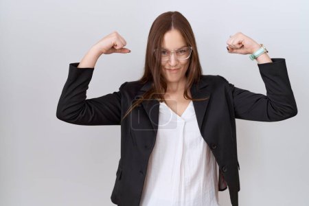 Téléchargez les photos : Belle femme brune portant une veste d'affaires et des lunettes montrant les muscles des bras souriant fière. concept de fitness. - en image libre de droit
