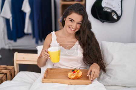 Photo for Young hispanic woman having breakfast sitting on bed at bedroom - Royalty Free Image
