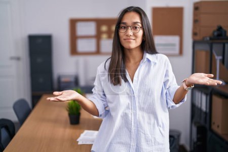 Photo for Young hispanic woman at the office clueless and confused with open arms, no idea concept. - Royalty Free Image