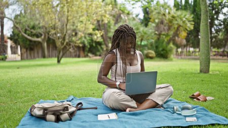 Téléchargez les photos : Étudiante afro-américaine utilisant un ordinateur portable assis sur le sol à l'université du campus - en image libre de droit