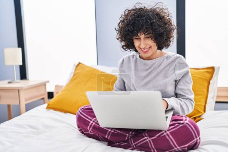 Téléchargez les photos : Young middle east woman using laptop sitting on bed at bedroom - en image libre de droit