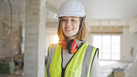 Foto de Joven mujer rubia arquitecta sonriendo confiada de pie en el sitio de construcción - Imagen libre de derechos
