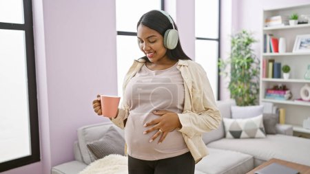 Photo for Laughing & carefree, young pregnant woman, casually touching her belly, dancing and listening to music while enjoying a morning coffee at home - Royalty Free Image