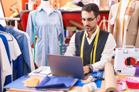 Photo for Young hispanic man tailor using laptop at atelier - Royalty Free Image