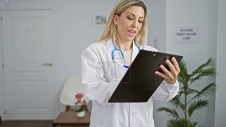 Photo for Young blonde woman doctor writing medical report at clinic waiting room - Royalty Free Image