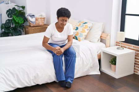 Téléchargez les photos : Femme afro-américaine souffrant d'une blessure au genou assise sur le lit dans la chambre - en image libre de droit