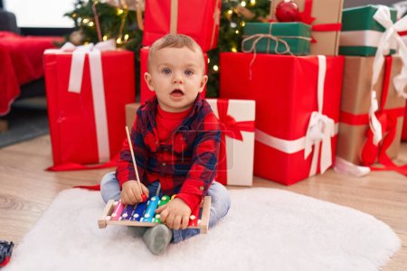 Téléchargez les photos : Adorable blond tout-petit jouant xylophone assis sur le sol par des cadeaux de Noël à la maison - en image libre de droit