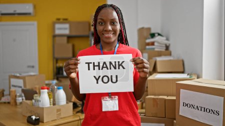 Photo for Beautiful african american woman volunteer, cheerfully welcoming with a smile, pointing at you from the bustling charity center - Royalty Free Image
