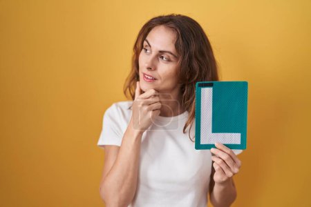 Photo for Beautiful brunette woman holding l sign for new driver serious face thinking about question with hand on chin, thoughtful about confusing idea - Royalty Free Image