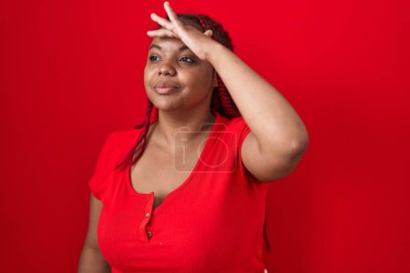 Photo for African american woman with braided hair standing over red background very happy and smiling looking far away with hand over head. searching concept. - Royalty Free Image