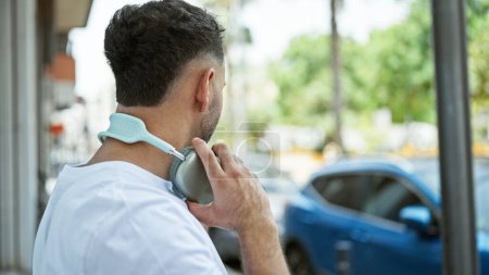 Téléchargez les photos : Jeune homme arabe portant des écouteurs debout à l'arrière dans la rue - en image libre de droit