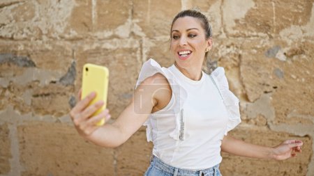 Foto de Young blonde woman smiling confident making selfie by the smartphone at street - Imagen libre de derechos