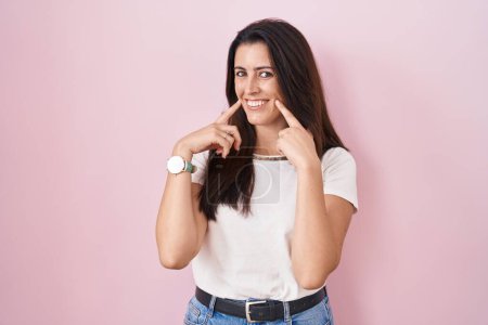 Téléchargez les photos : Jeune femme brune debout sur fond rose souriant avec la bouche ouverte, les doigts pointant et forçant sourire joyeux - en image libre de droit