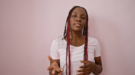 Foto de Cool mujer afroamericana de pie relajado, mostrando sus hermosas trenzas, y hablando en serio sobre un fondo rosa aislado - Imagen libre de derechos
